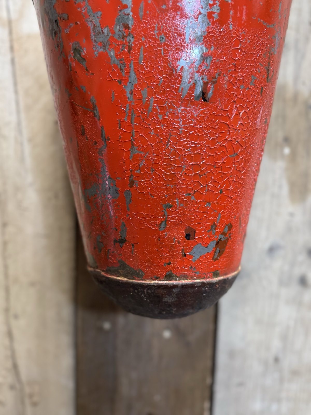 A weathered red fire extinguisher with chipped paint shown on the back side of a vintage galvanised hanging fire bucket planter