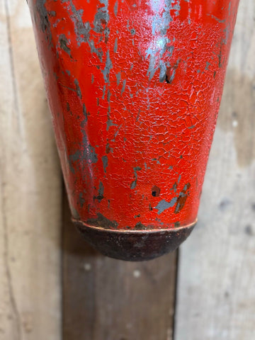 A weathered red fire extinguisher with chipped paint shown on the back side of a vintage galvanised hanging fire bucket planter