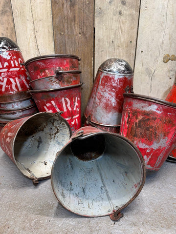 Vintage rusty red enamel fire bucket with faded white lettering and metal handle used as hanging planter pot