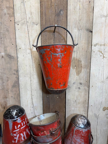 Vintage red metal fire bucket with black handle showing chipped paint used as hanging planter or fire pail