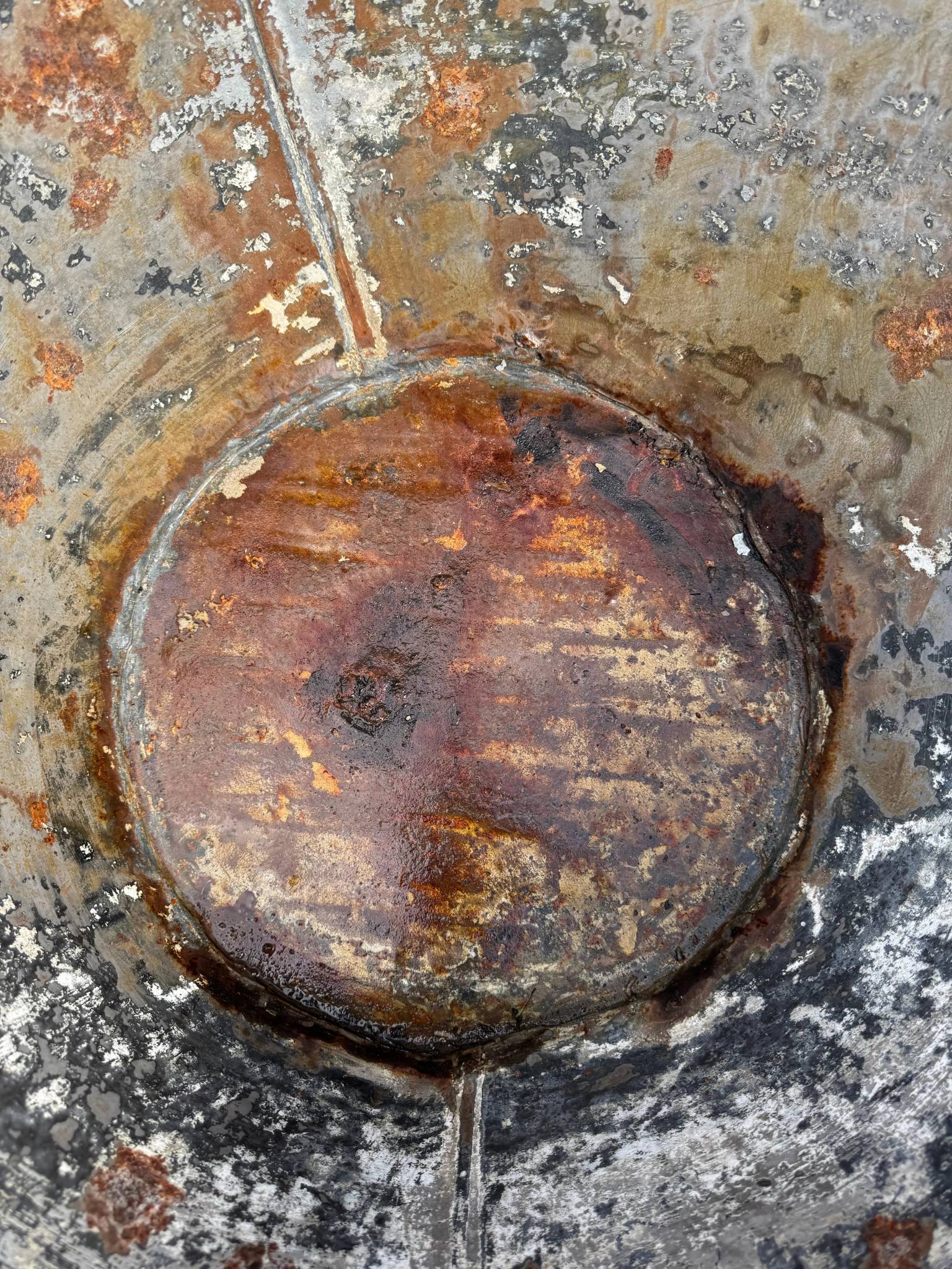 A weathered circular manhole cover showing rust on a galvanised metal bath tub garden planter vintage rustic display