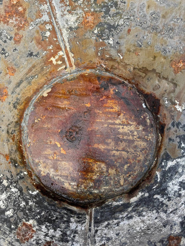 A weathered circular manhole cover showing rust on a galvanised metal bath tub garden planter vintage rustic display