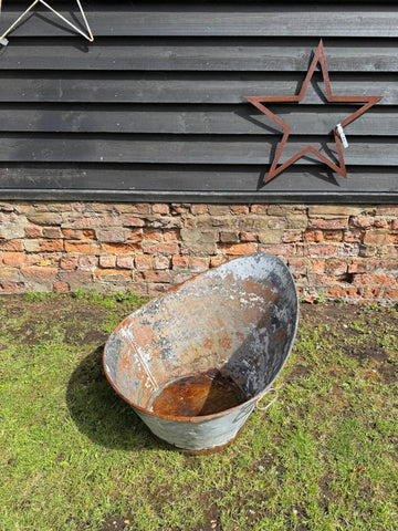 Weathered oval-shaped vintage galvanised metal bath with rust patches and peeling paint for garden display