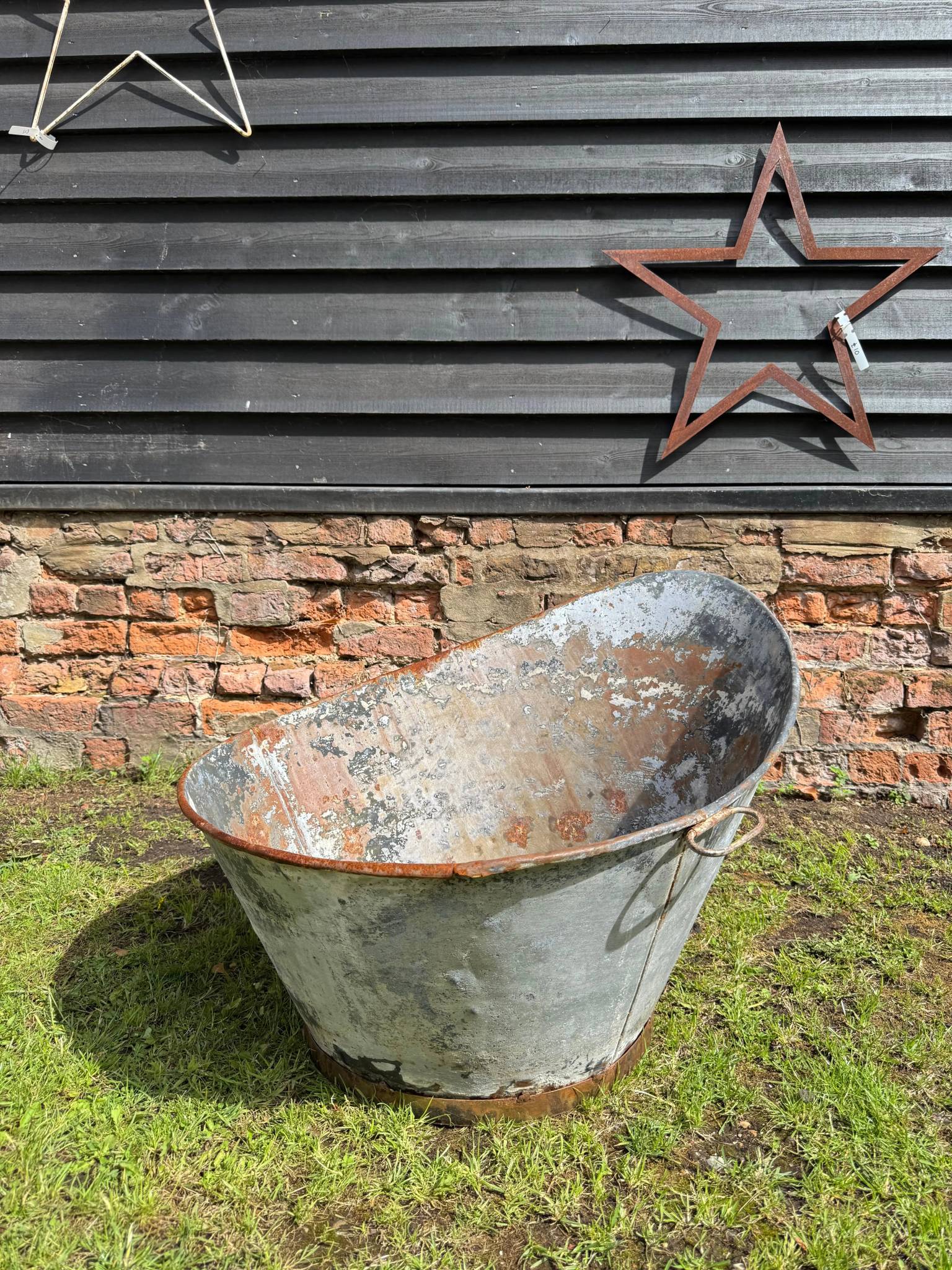 Vintage galvanised metal bath tub garden planter with rust-streaked weathered oval shape and two small handles