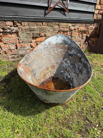 Rusty weathered triangular metal wheelbarrow with peeling paint next to vintage galvanised metal bath tub garden planter