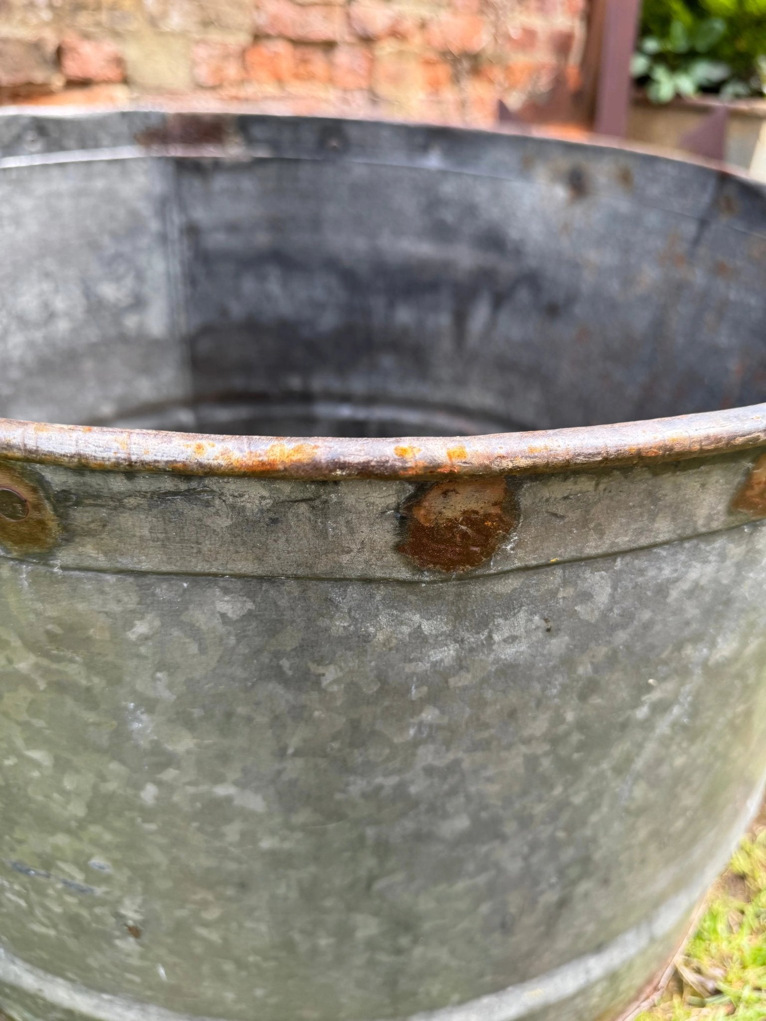Vintage galvanised metal round garden planter tub with rust stains and rivets for a rustic outdoor look