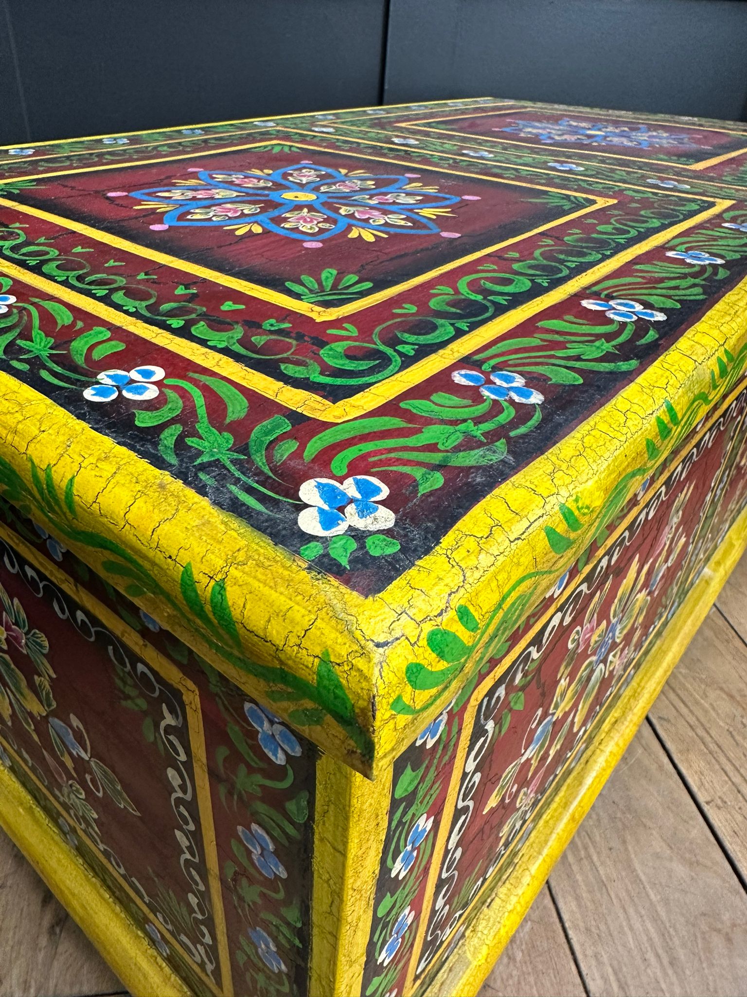 Vintage indian hand painted wooden trunk with cracked yellow trim and floral patterns used as coffee table