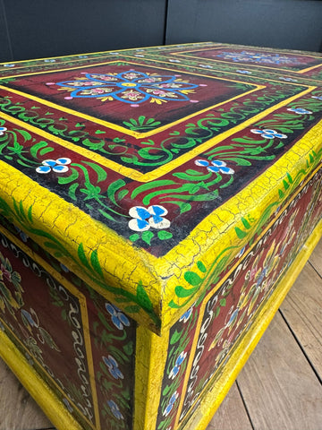 Vintage indian hand painted wooden trunk with cracked yellow trim and floral patterns used as coffee table