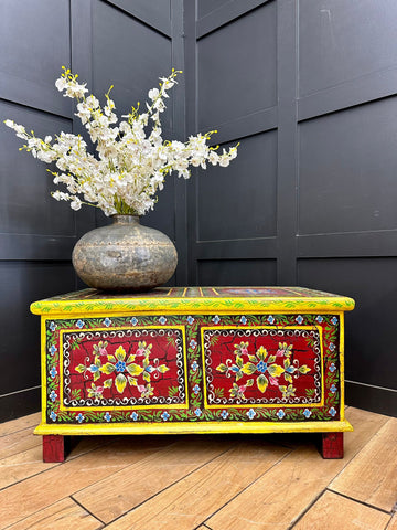 Vintage indian hand painted wooden chest in vibrant yellow and red with floral designs used as coffee table