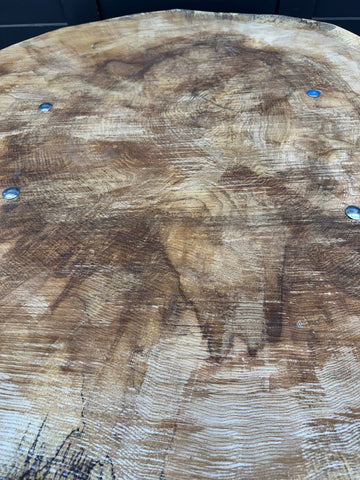A rustic round wooden dining table with maple top and cast iron base featuring four metallic fasteners