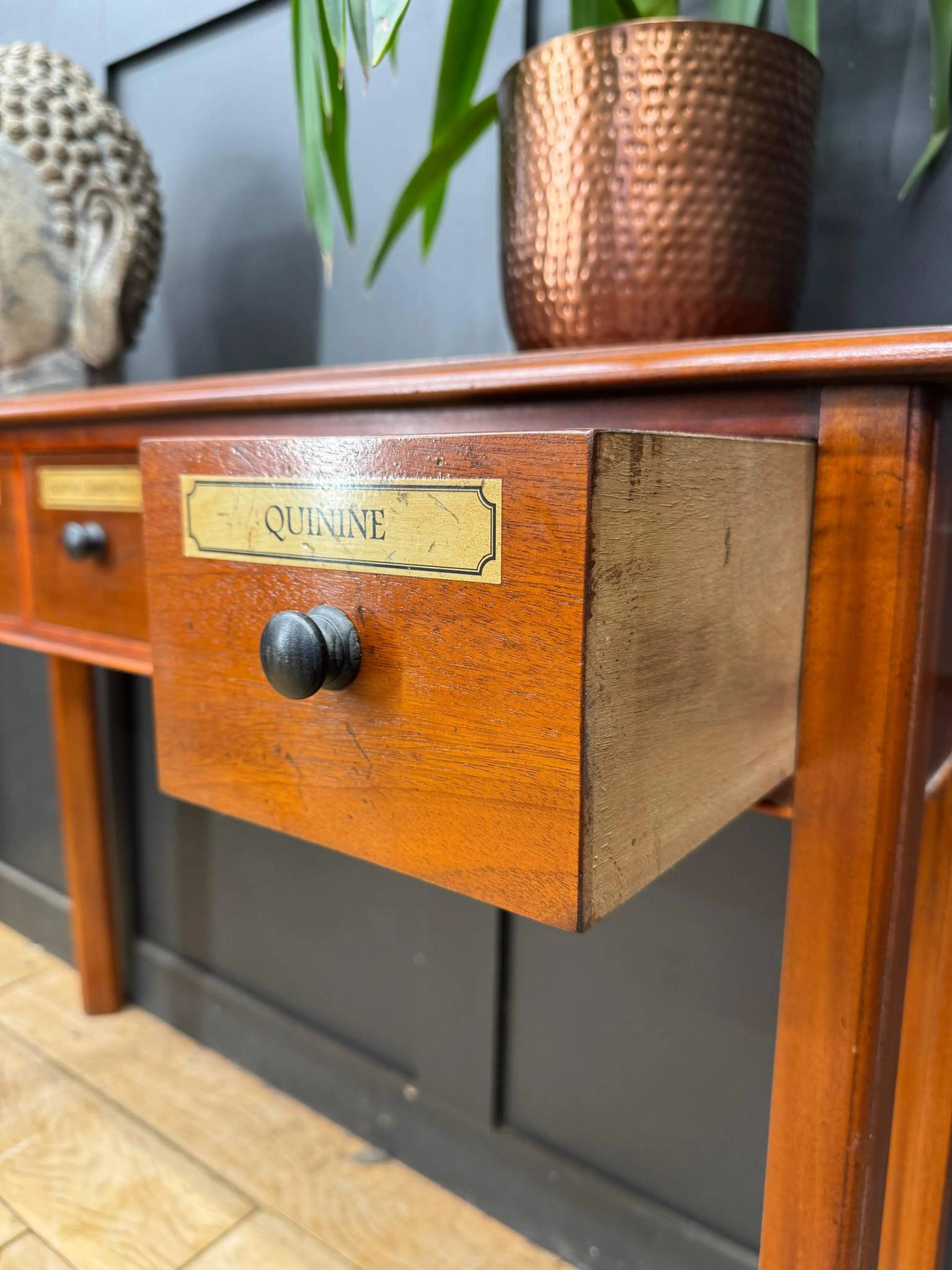 Vintage mahogany apothecary style console table with black round knobs and quinine labeled drawer in wood finish