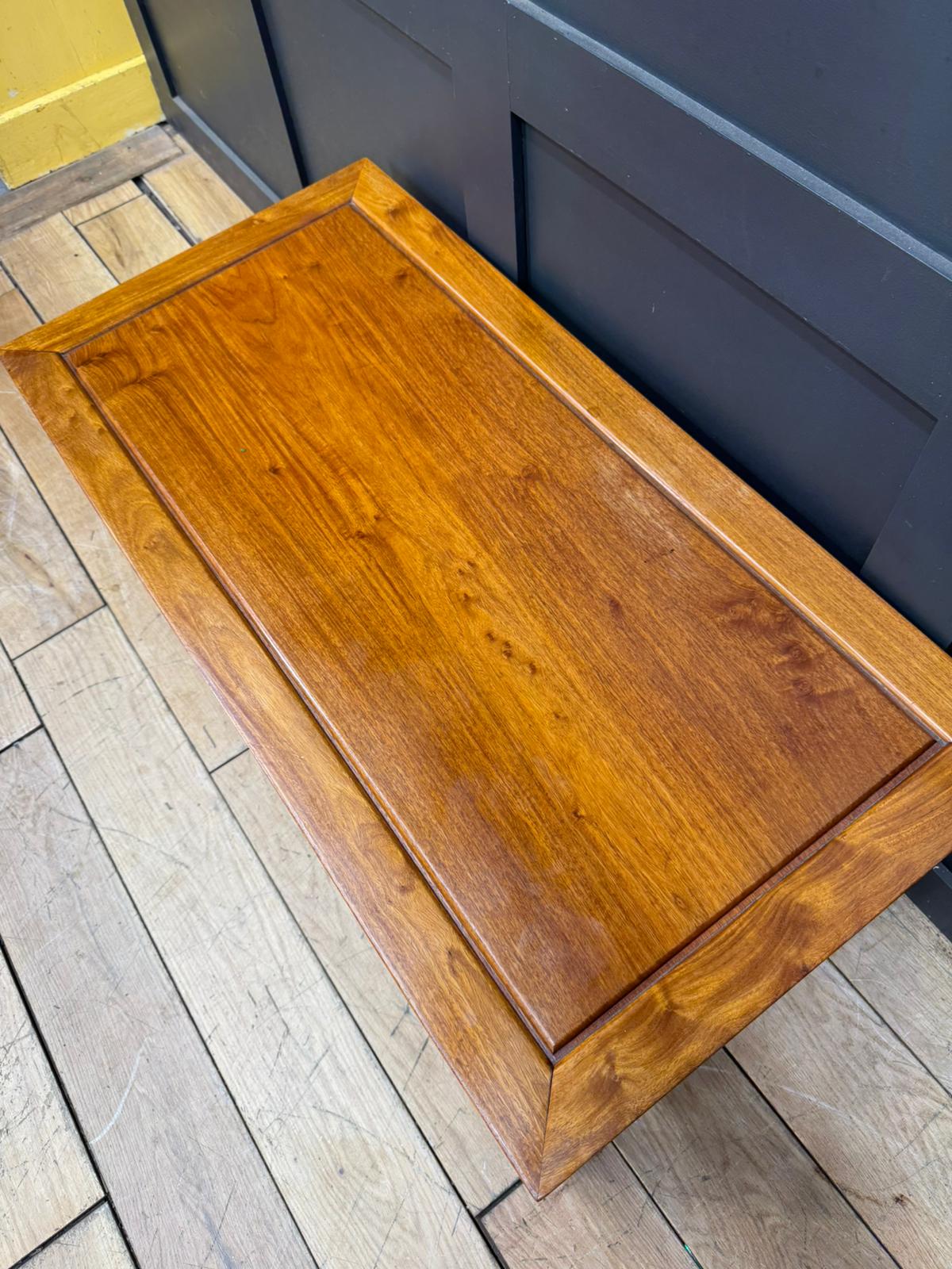 A polished golden brown wooden storage bench with raised edges perfect as a vintage mahogany coffee table
