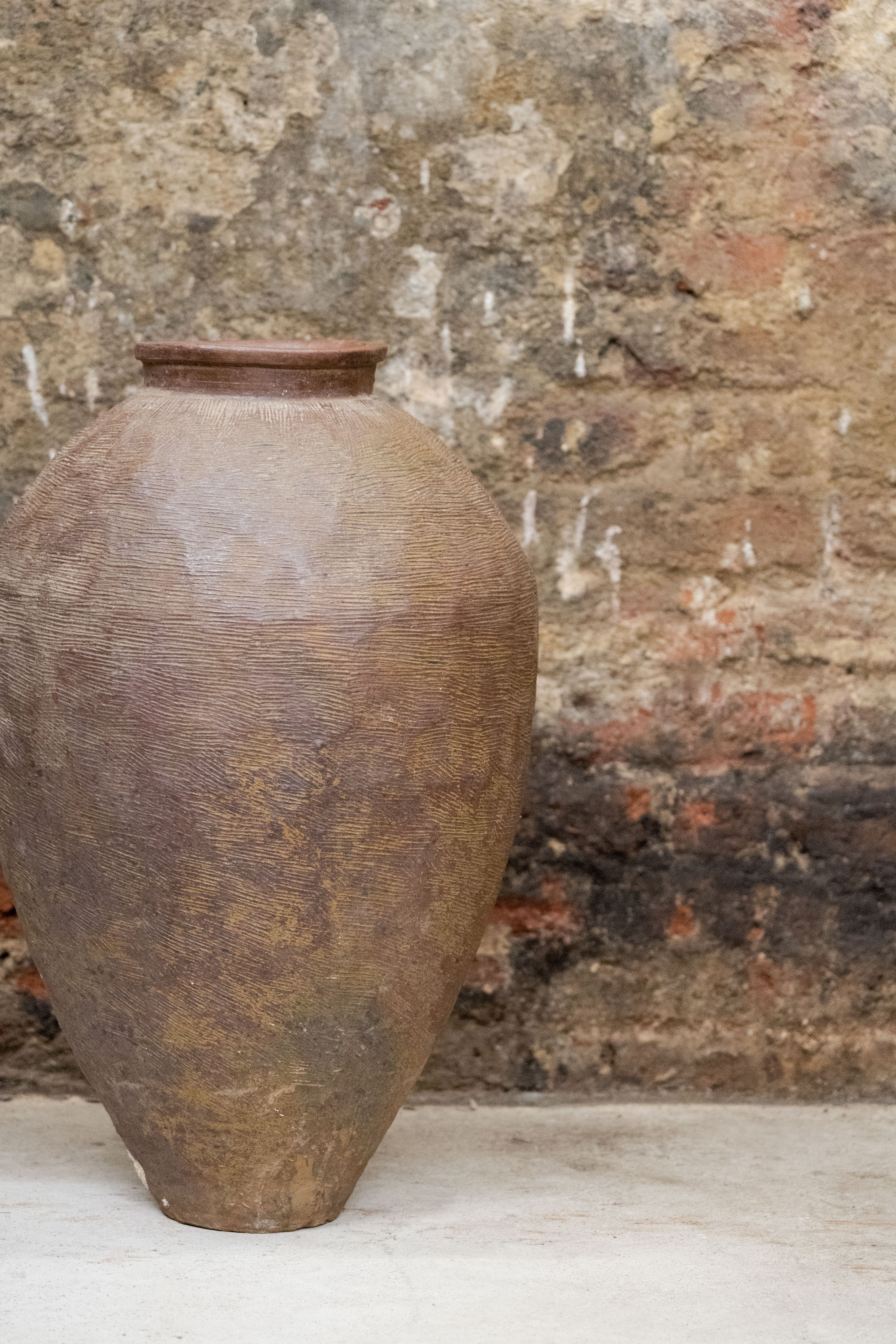 A vintage old brown asian pot made of rustic ceramic with a textured handcrafted surface and a tapered neck