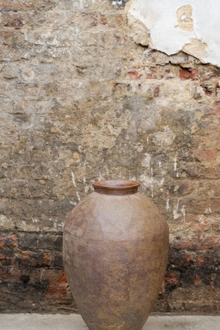 A vintage old brown asian pot made of rustic ceramic with a textured ribbed surface and a wider rim