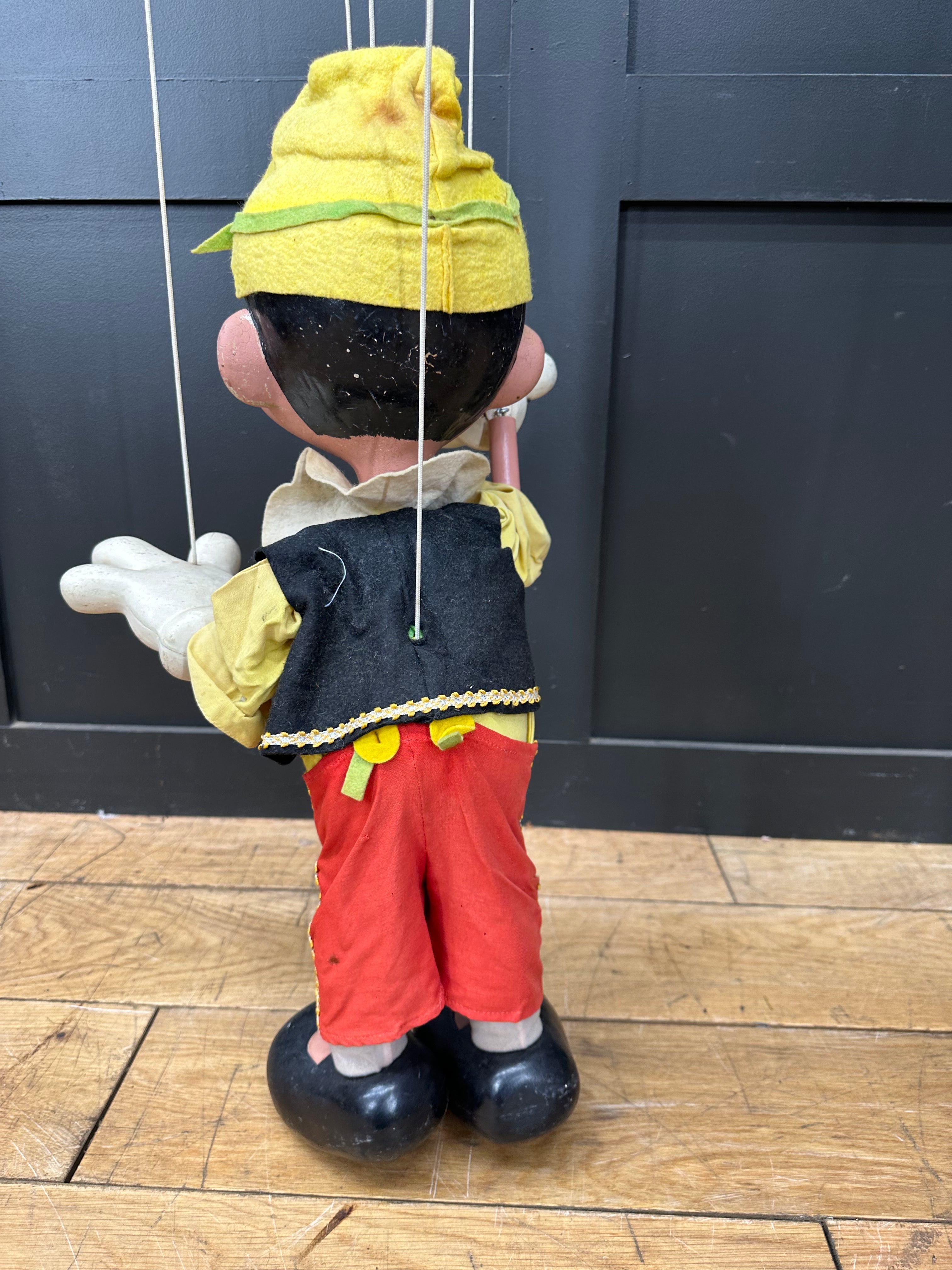 Vintage pelham puppets string-puppet pinocchio with yellow hat green trim black vest and red trousers standing on black shoes