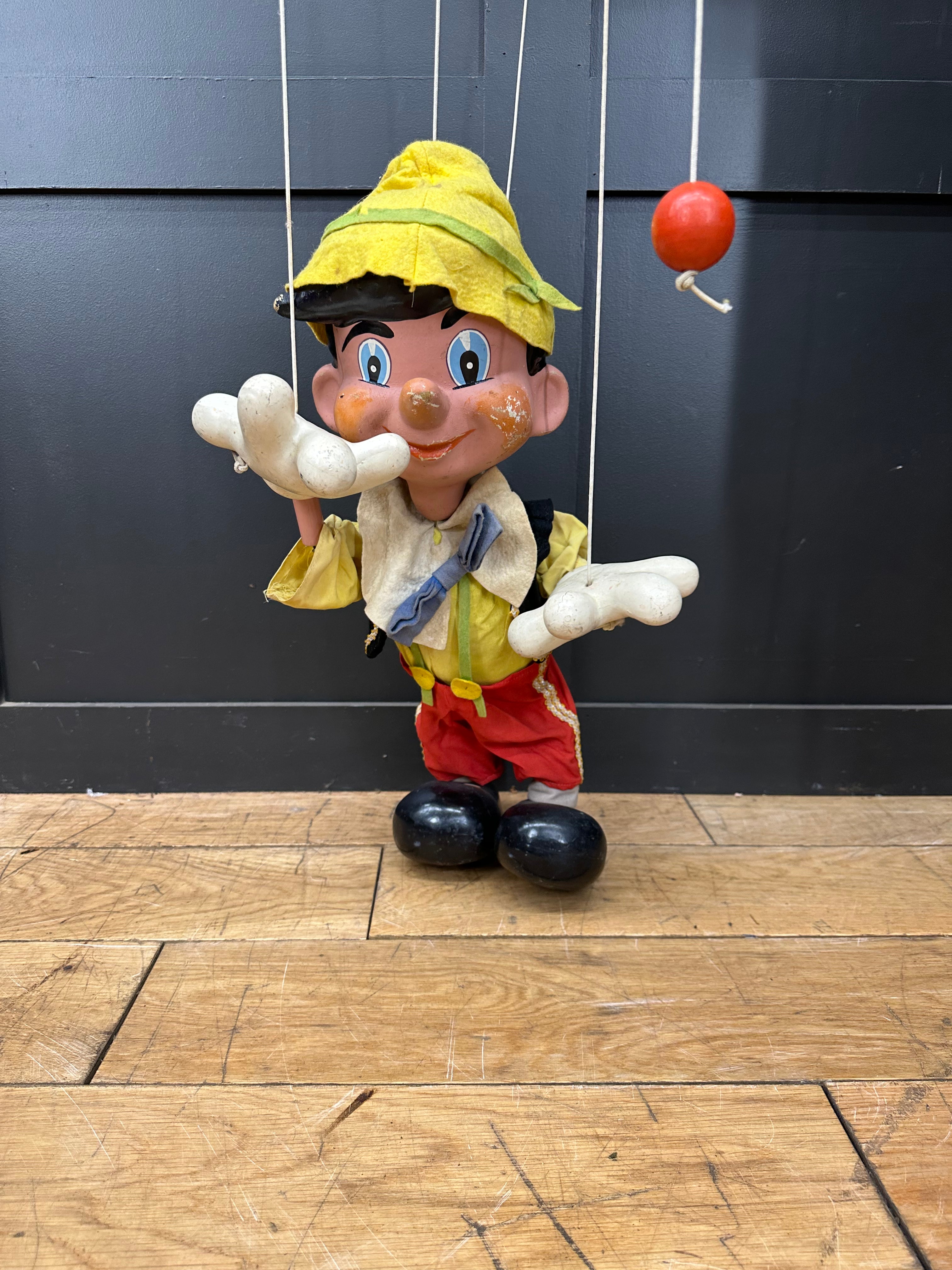 Vintage pelham puppets pinocchio marionette with yellow hat red trousers and painted face standing on wooden floor