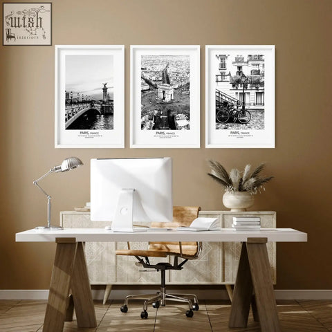 Three framed black and white paris wall art prints with white borders hanging above a desk vintage posters travel set