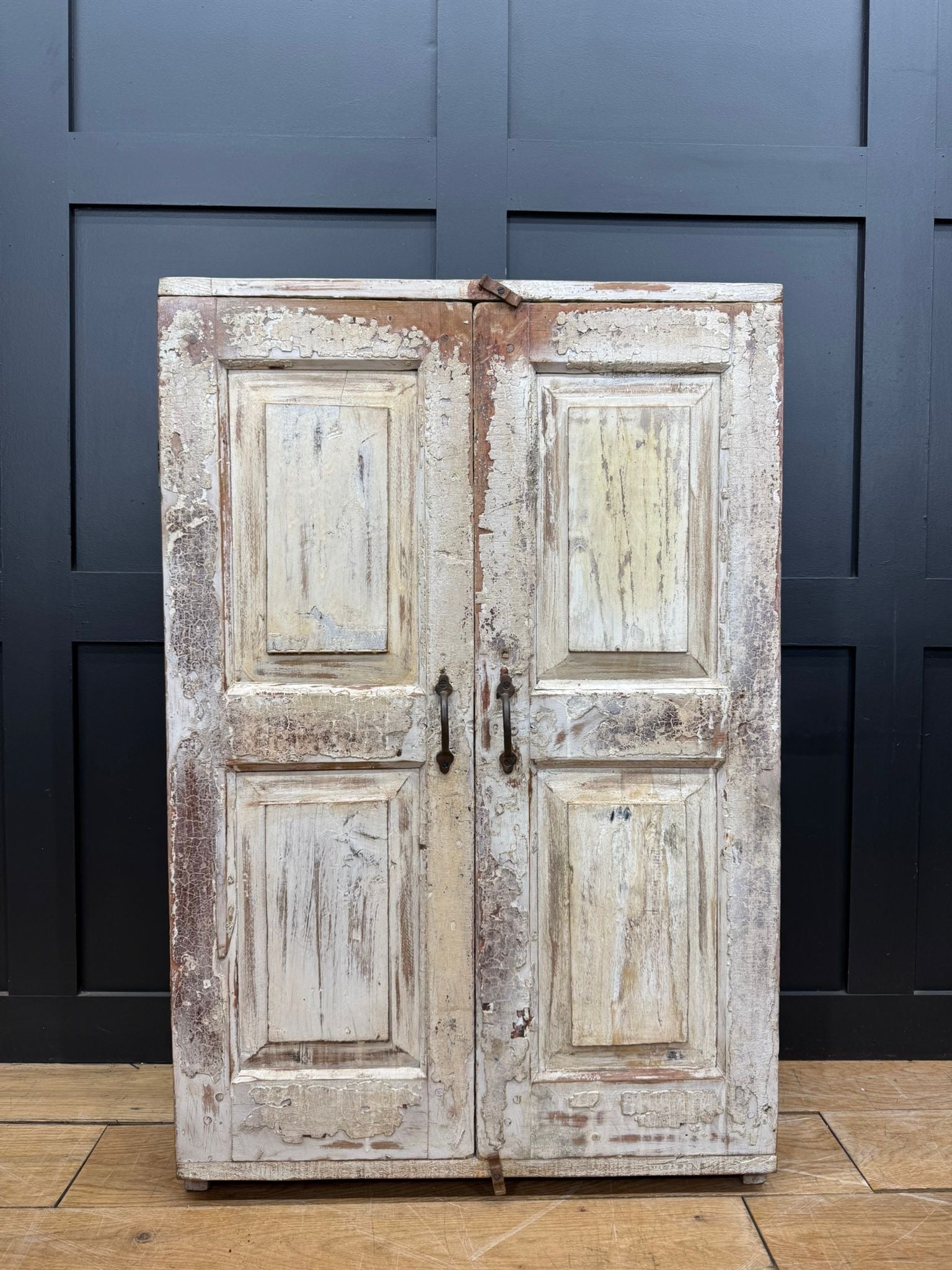 Weathered white painted wooden double doors with peeling paint and rustic black metal handles on vintage rustic cupboard
