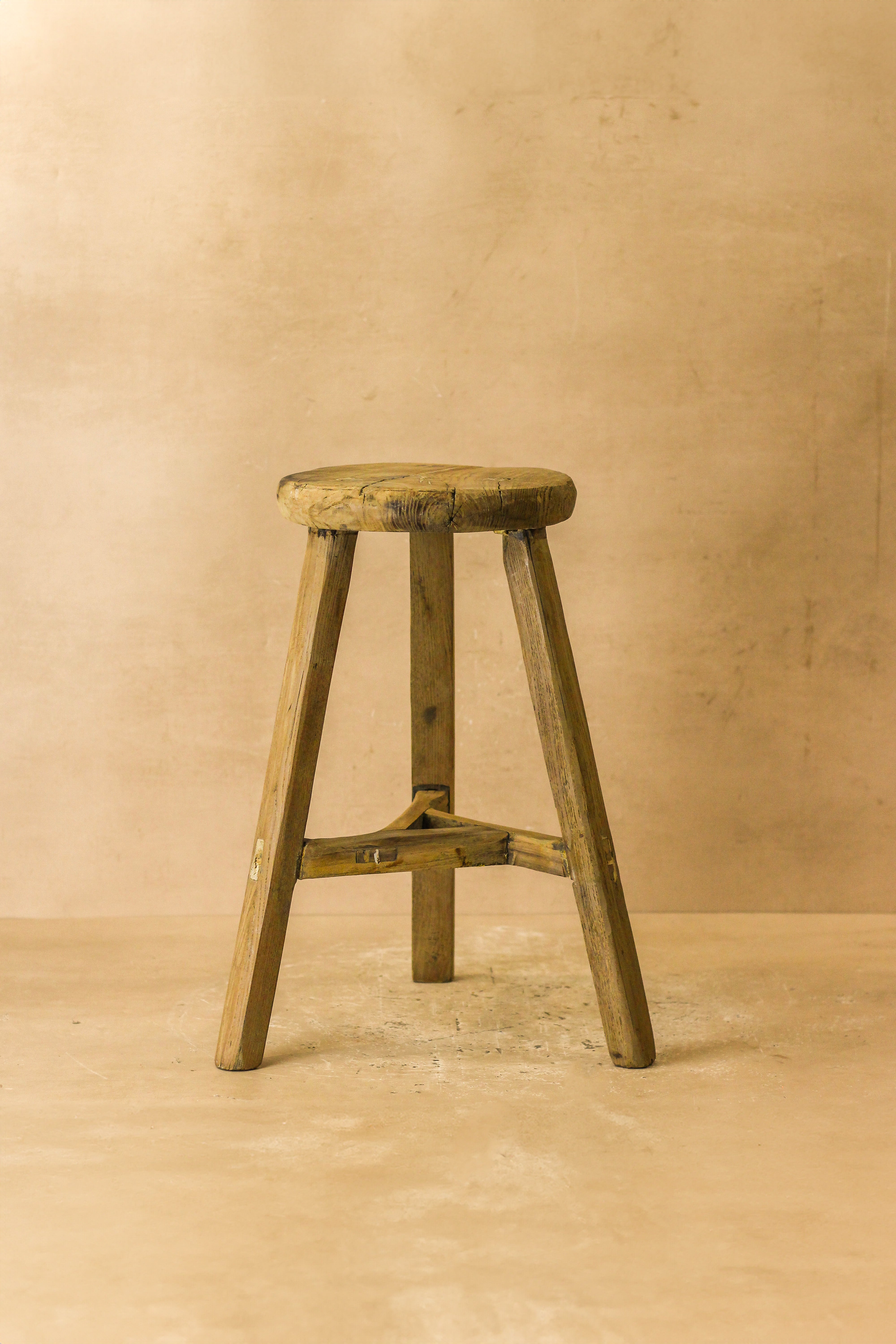 Vintage rustic elm wood stool with a round weathered seat and three angled legs joined by a central crossbar wood stool