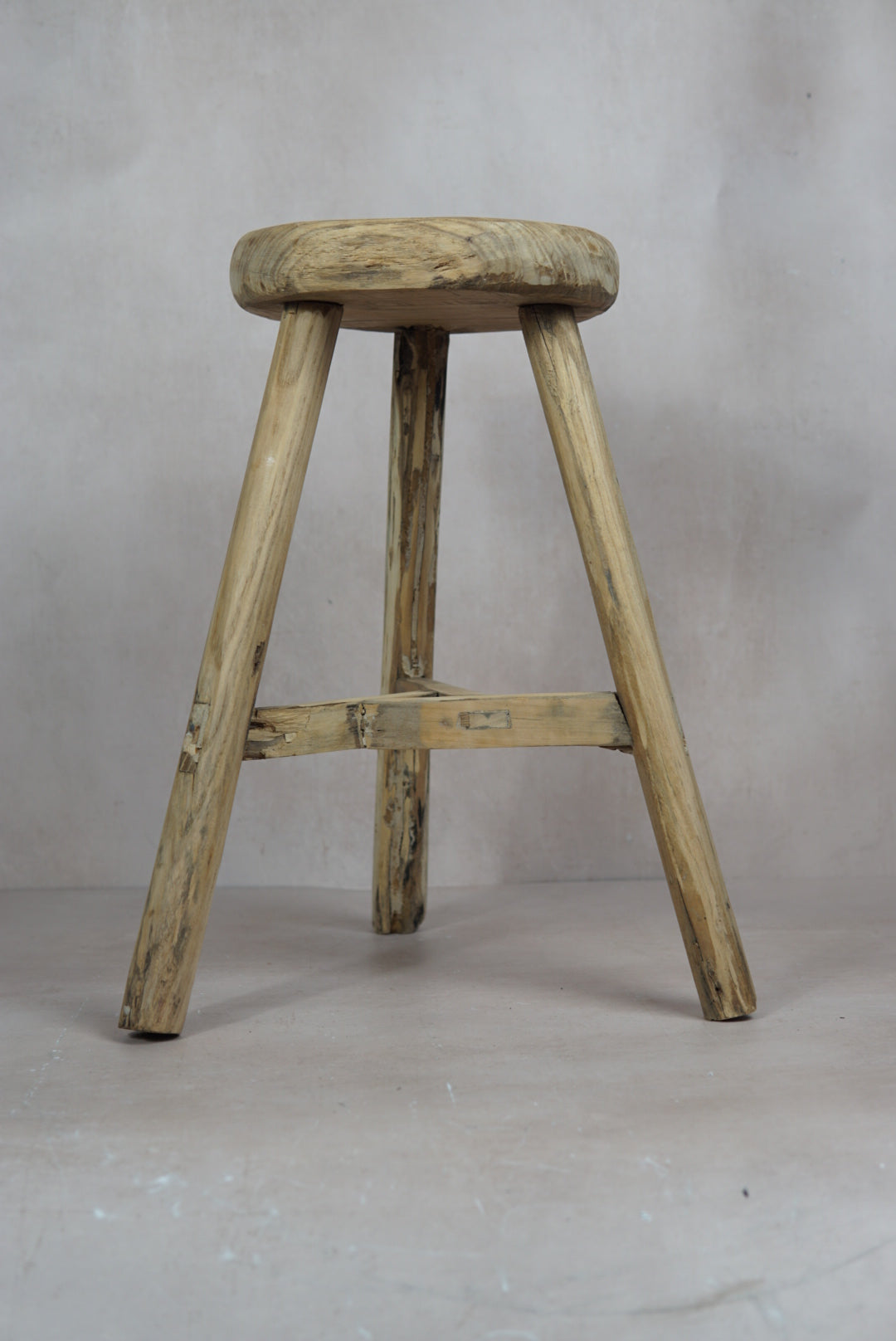 Vintage rustic elm wood stool with a round weathered seat and three sturdy legs connected by a support beam