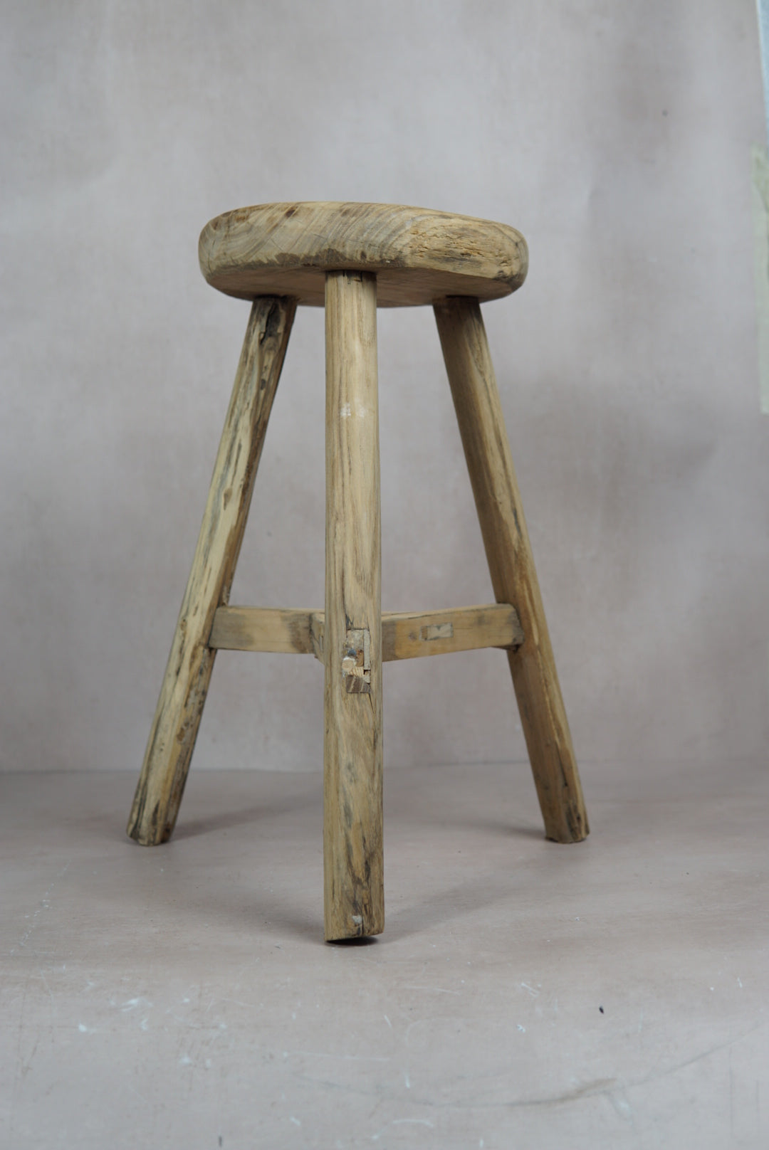 Vintage rustic elm wood stool with a round weathered seat and three sturdy legs connected by a crossbar