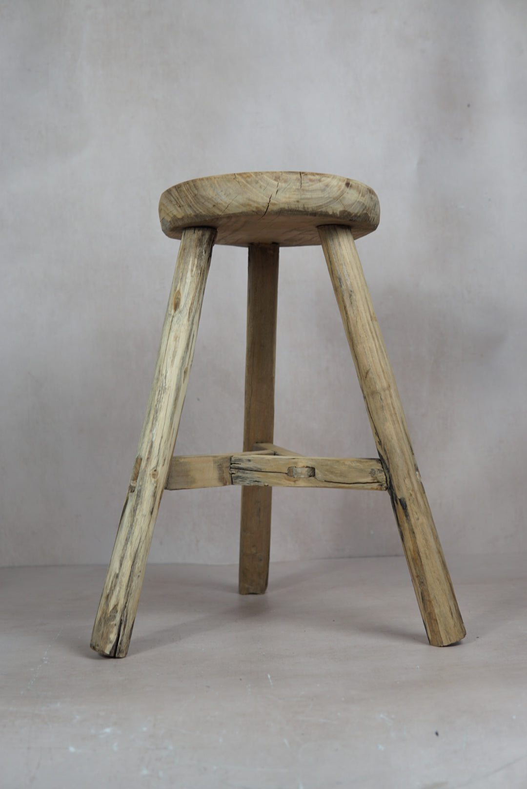 Vintage rustic elm wood stool with a round weathered seat and three sturdy legs connected by a crossbar