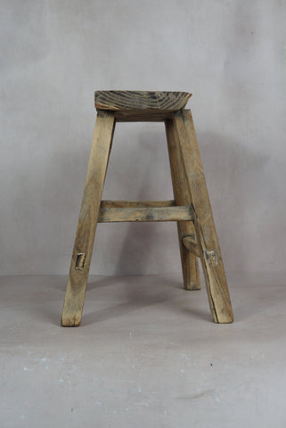 Vintage rustic stool made of elm wood with a weathered light brown finish and visible wood grain