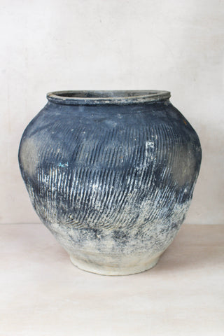 A vintage textured grey ceramic jar with vertical ridges and a faded white base perfect for rustic decor