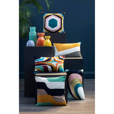 Vibrant geometric-patterned throw pillows in bold colors next to a visage small yellow face vase for modern decor