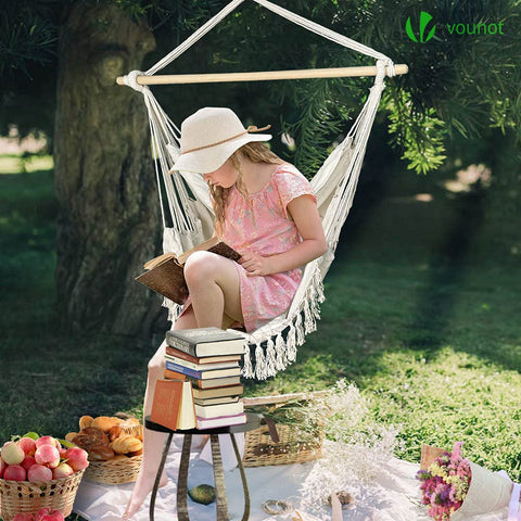White macrame hammock swing chair with wooden spreader bar and fringe in beige for indoor and outdoor use