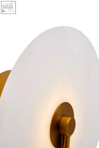 Gold-toned wall sconce with frosted white circular glass shade for white marble wall accents in the waldorf collection
