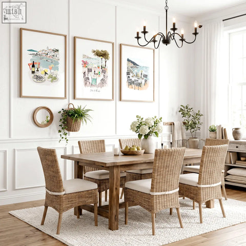 Woven wicker dining chairs with light beige cushions and wooden legs in a dining room with mediterranean coastal wall art three prints