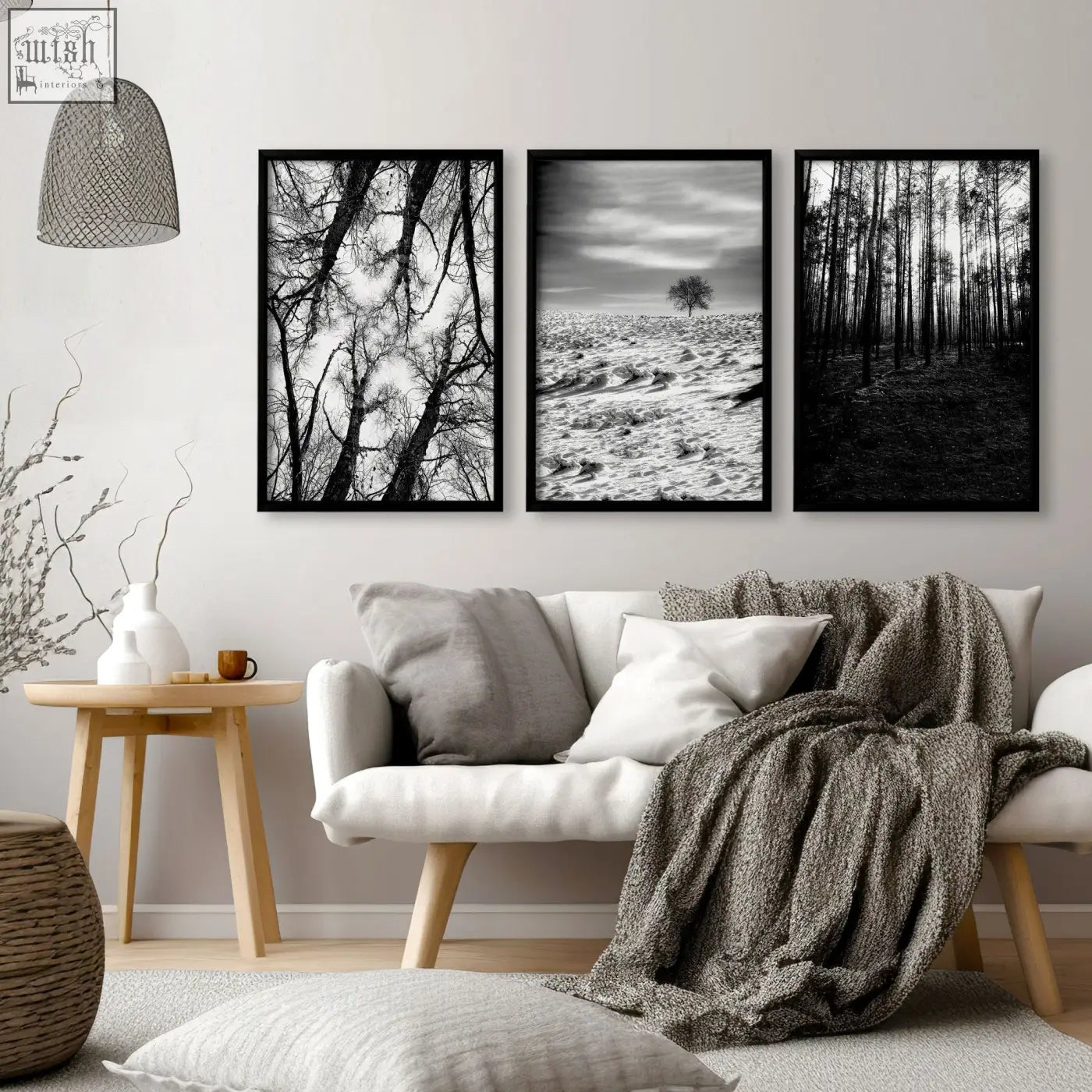 Three black-framed black and white forest and winter landscape wall art prints hang above a white sofa on grey walls living room