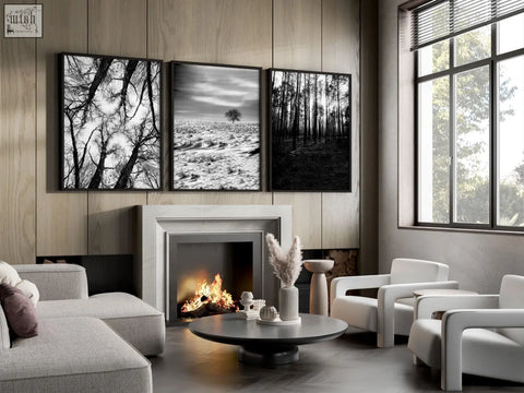 Three black and white framed wall art prints of forest and winter landscapes hanging above a fireplace on grey walls living room