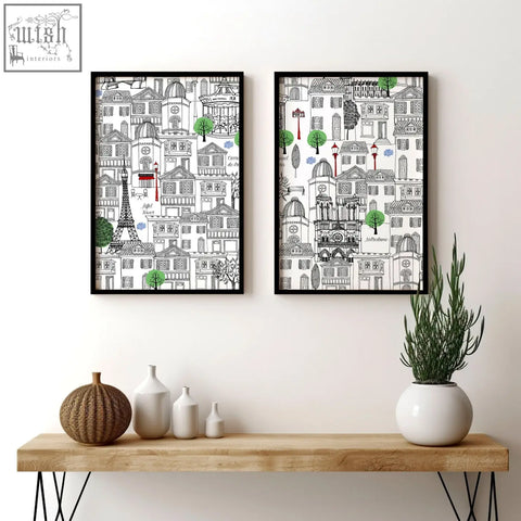 Two black-framed wall art paris prints with detailed european cityscape line drawings and green red accents above wood table