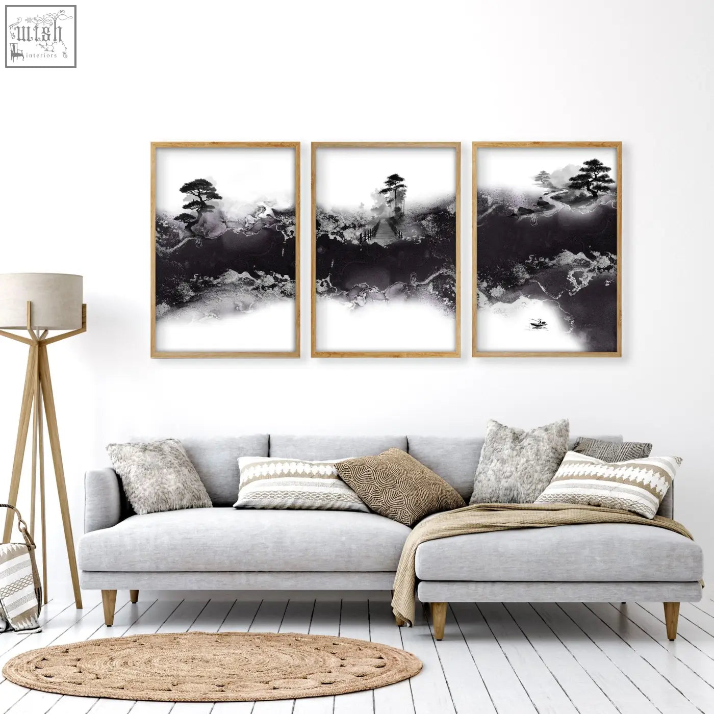 Three framed black and white ink wash landscape art prints with wooden frames hang above a gray sofa in high ceiling living room