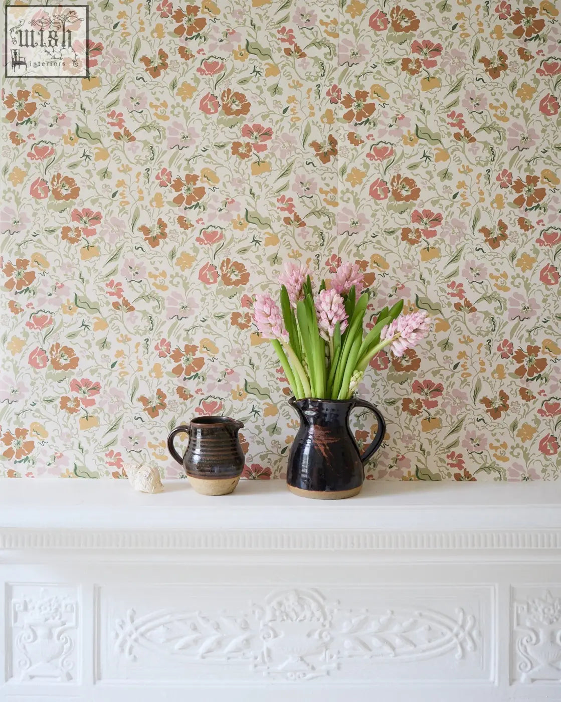 Dark ceramic pitcher with glossy finish holding pink hyacinths featured in wandle wilde wallpaper earth with oversized floral
