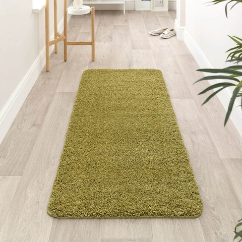A washable olive green shaggy rug with a soft textured surface on light wood flooring perfect for cozy spaces