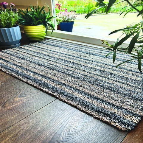 A washable ribbon mat with gray and white stripes and a woven fibrous surface on dark wood flooring