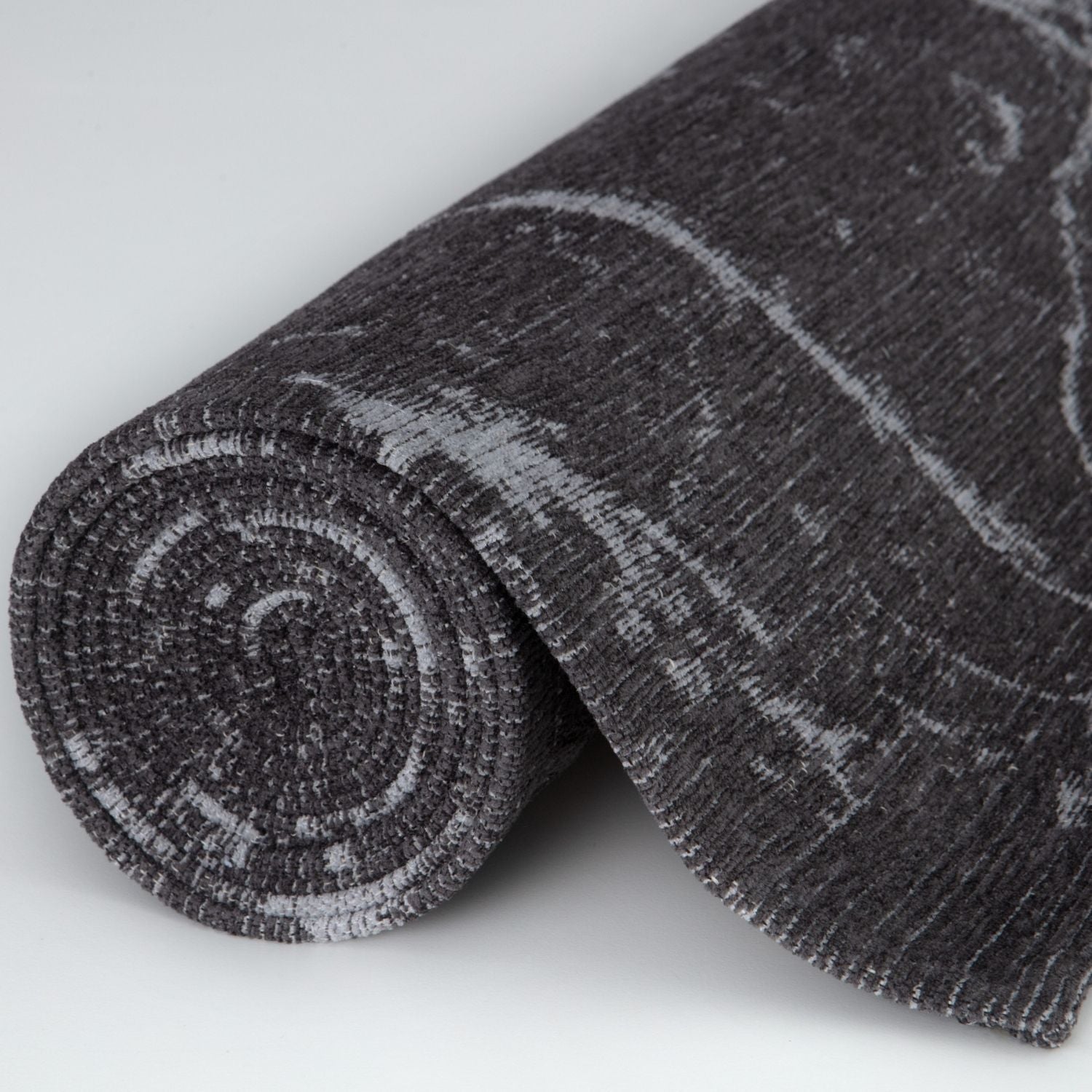 A rolled-up washable rug carina dark grey with a subtle abstract pattern and textured weave in dark grey tones
