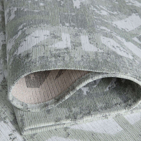 A textured, washable rug carina green rolled up with a muted gray and white abstract pattern