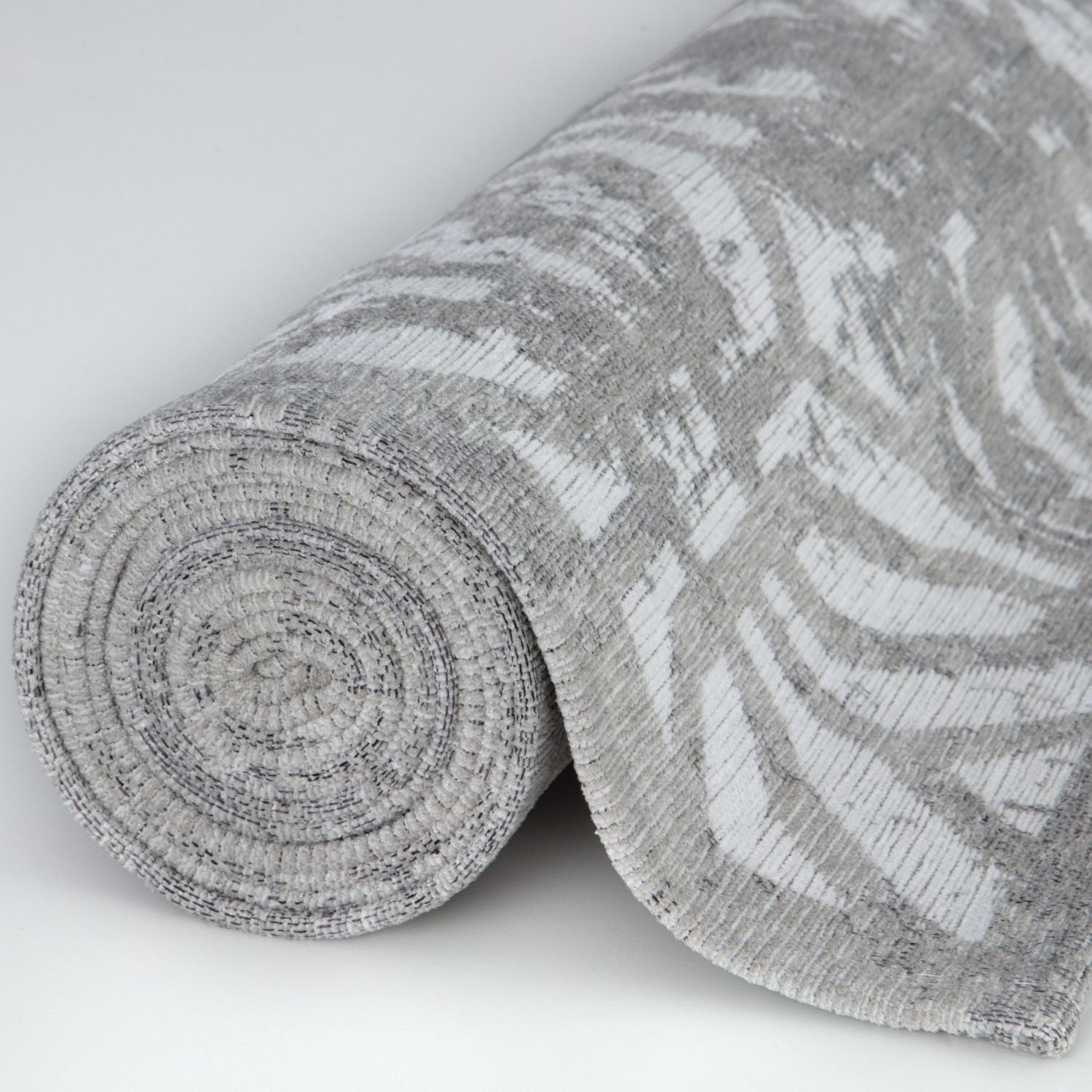 A rolled-up washable rug carina grey in textured grey with a subtle abstract leaf pattern