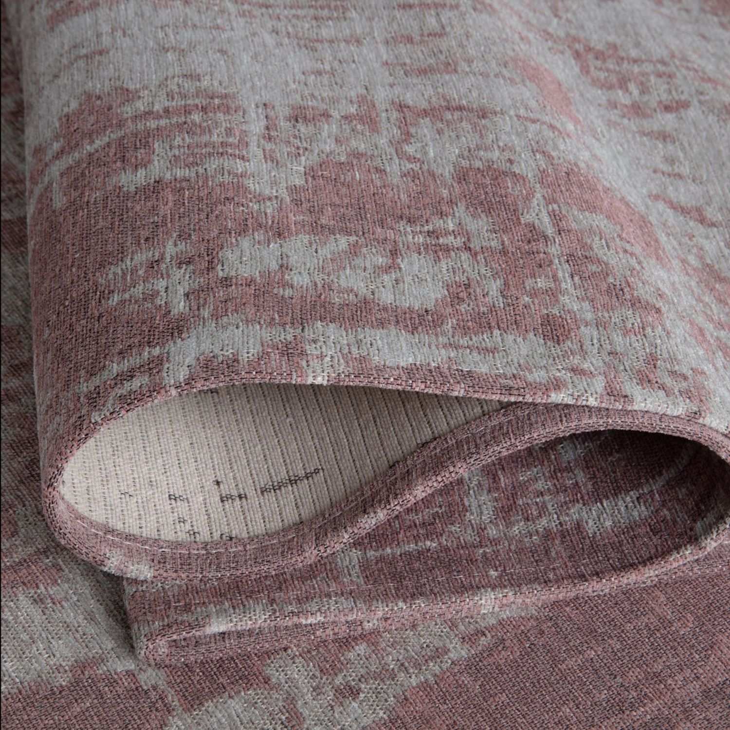 A rolled-up washable rug carina in pink with a faded distressed pattern in muted gray and pink tones