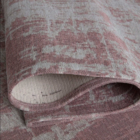 A rolled-up washable rug carina in pink with a faded distressed pattern in muted gray and pink tones