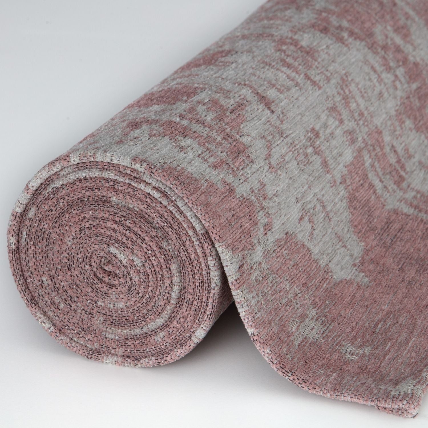 A rolled-up washable rug carina with a soft pink and gray abstract pattern and textured weave
