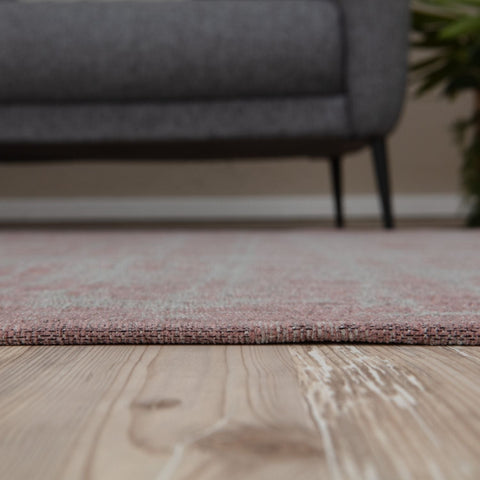 A soft pink washable rug carina with a subtle woven pattern on light wood flooring perfect for any room