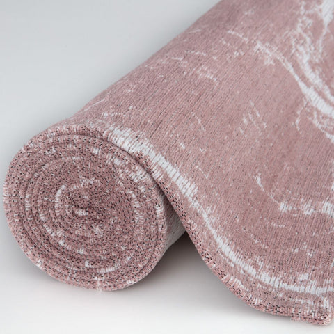 A rolled-up pink and white marbled knit washable rug carina made of textured woven fabric perfect for easy cleaning