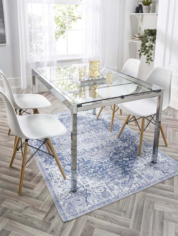 Modern glass-top dining table with sleek chrome legs on eterna blue washable rug for easy cleaning and style