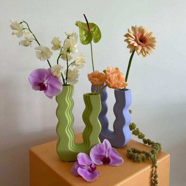 Three wavy pastel ceramic vases in green blue and lavender holding orchids gerberas and mixed flowers