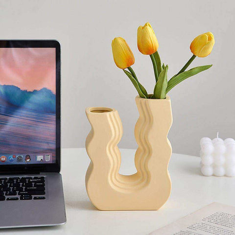 Cream-colored ceramic wavy wonder vase with a modern design holding bright yellow tulips